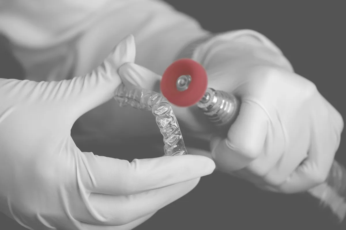 A dental technician polishing a clear aligner with a rotary tool in a laboratory.