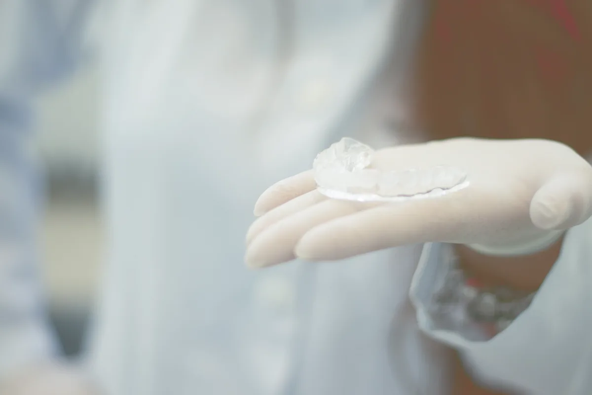A clear removable retainer held in a gloved hand.